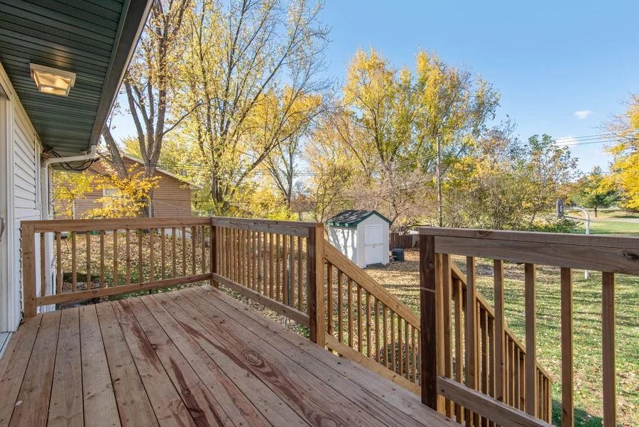 A wooden backyard deck with railings beside a landscaped lawn.