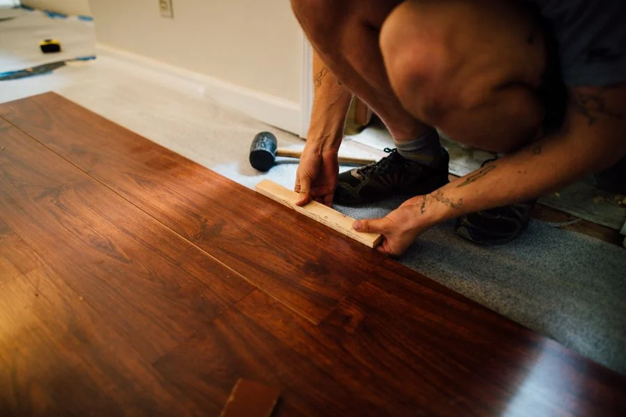 A flooring installer fitting wooden floorboards with a mallet.