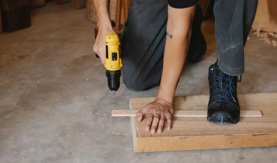 A tradesperson using a cordless drill to fasten a wooden board.